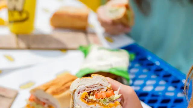 People holding Which Wich sandwiches at a park table