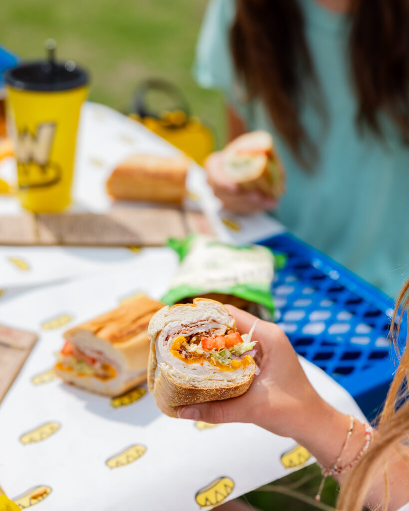 People holding Which Wich sandwiches at a park table