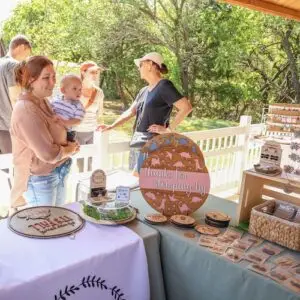 Woman holding a baby and standing behind a table with wares