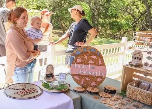 Woman holding a baby and standing behind a table with wares