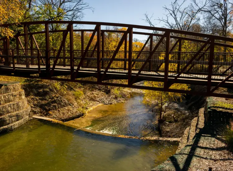 Cottonwood Creek Trail bridge spanning a creek with fall trees and sunlight in Allen, Texas.