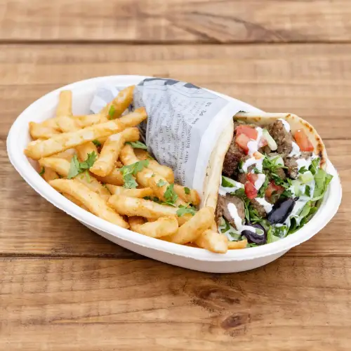 Wrap sandwich filled with meat and vegetables served with seasoned fries on a wooden table.