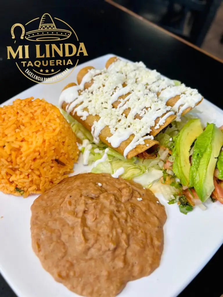 Plate of enchiladas topped with cheese sauce served with Mexican rice, refried beans, and avocado slices.