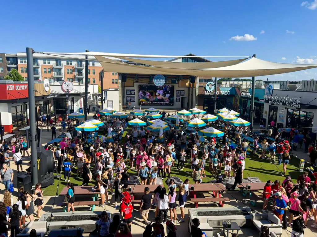 Large crowd gathered at The HUB in Allen, Texas with outdoor seating, umbrellas, and a stage for live entertainment.
