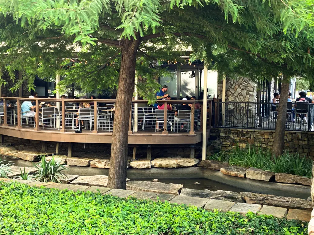 Outdoor patio dining area overlooking a creek with trees and seating at Watters Creek Village in Allen, Texas.