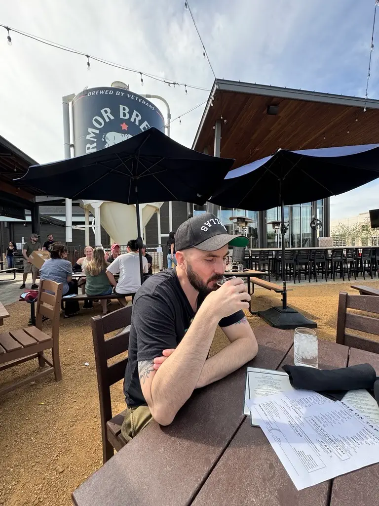 Man sitting at an outdoor patio table with drinks and menus at Armor Brewing Co. in Allen, Texas.