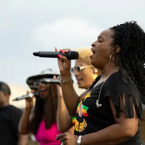 Female singer performing with a microphone alongside backup vocalists during a live music performance in Allen, Texas.