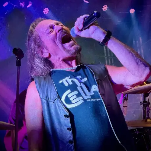 Male singer performing with a microphone on stage during a live rock concert under colorful stage lighting.
