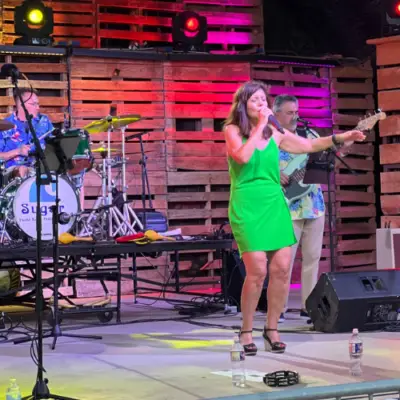 Female singer performing on stage with a live band under colorful lights during a concert.