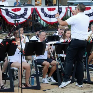 Conductor leading the Allen Philharmonic Orchestra during a patriotic outdoor concert performance at Watters Creek Village in Allen, Texas.