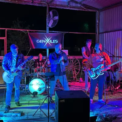 Members of the GenXiles band performing live on stage under colorful lights at an outdoor music venue.