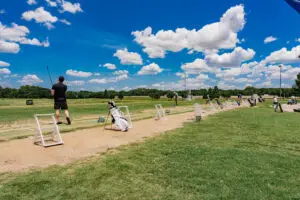 Golfers practicing at a driving range at The Courses at Watters Creek in Allen, Texas under a blue sky.