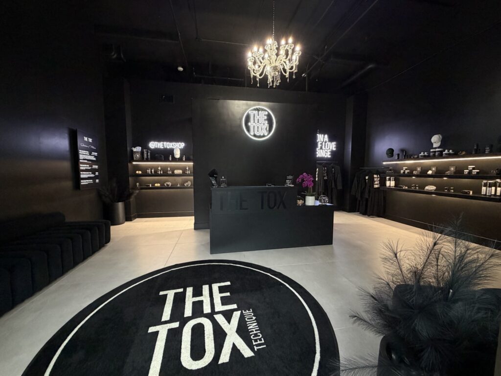 Interior of The Tox Allen wellness studio featuring a black modern reception area, chandelier lighting, and skincare displays.