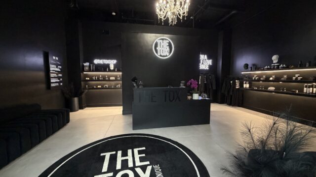 Interior of The Tox Allen wellness studio featuring a black modern reception area, chandelier lighting, and skincare displays.