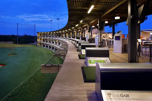 Rows of illuminated hitting bays at Topgolf in Allen, Texas during the evening.