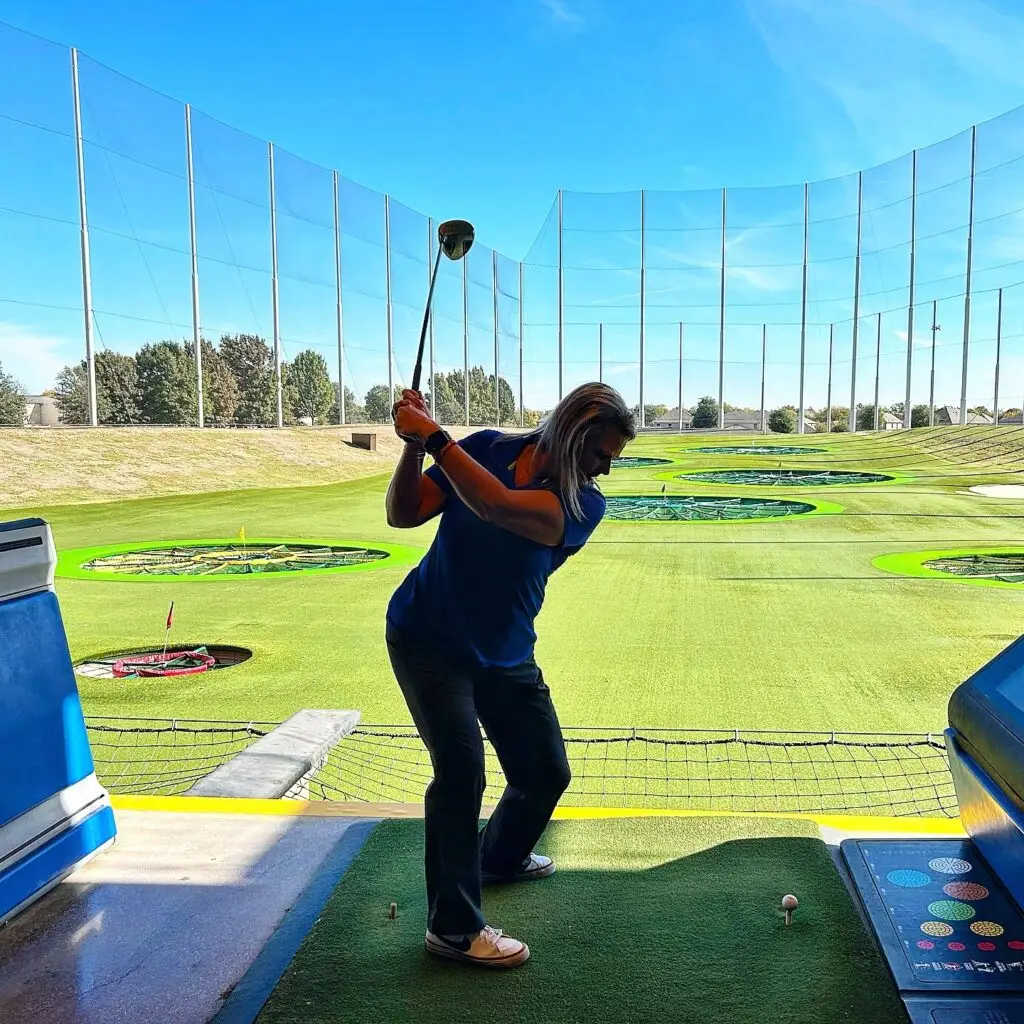 Person swinging a golf club at Topgolf in Allen, Texas with targets visible on the range.