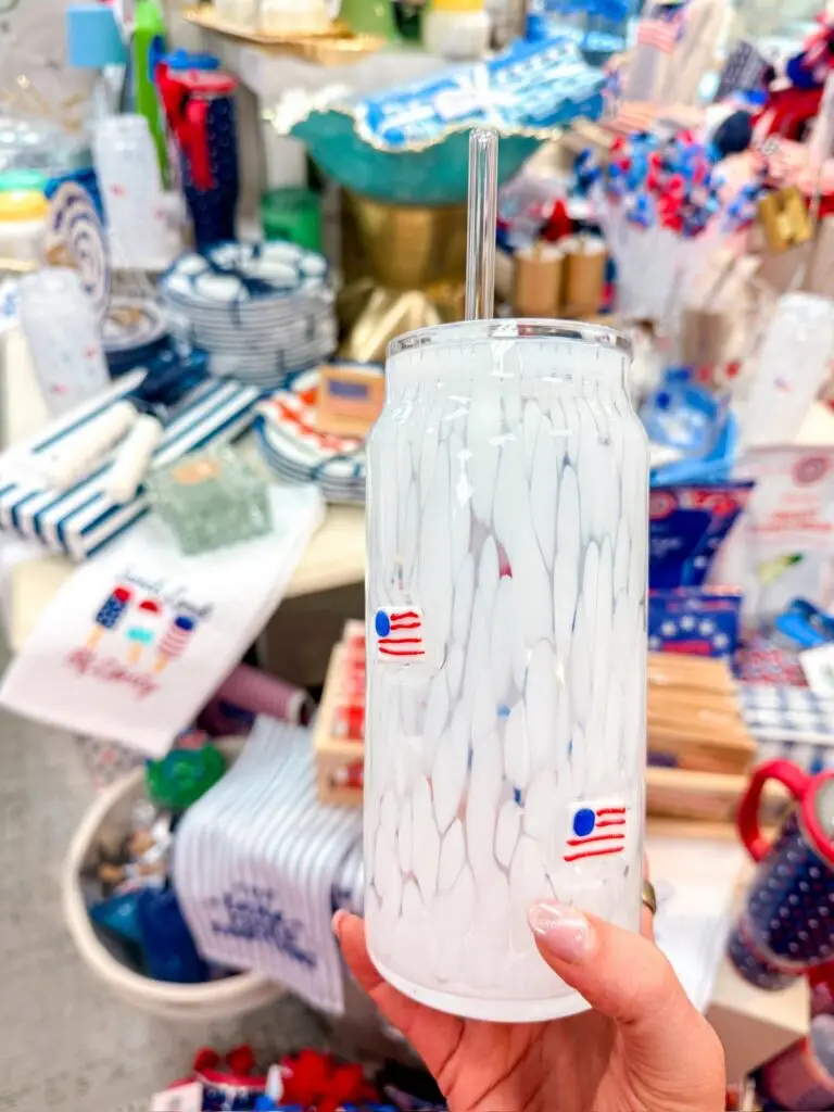 Hand holding a patriotic tumbler in front of red, white, and blue summer décor and party accessories at Hindy House.