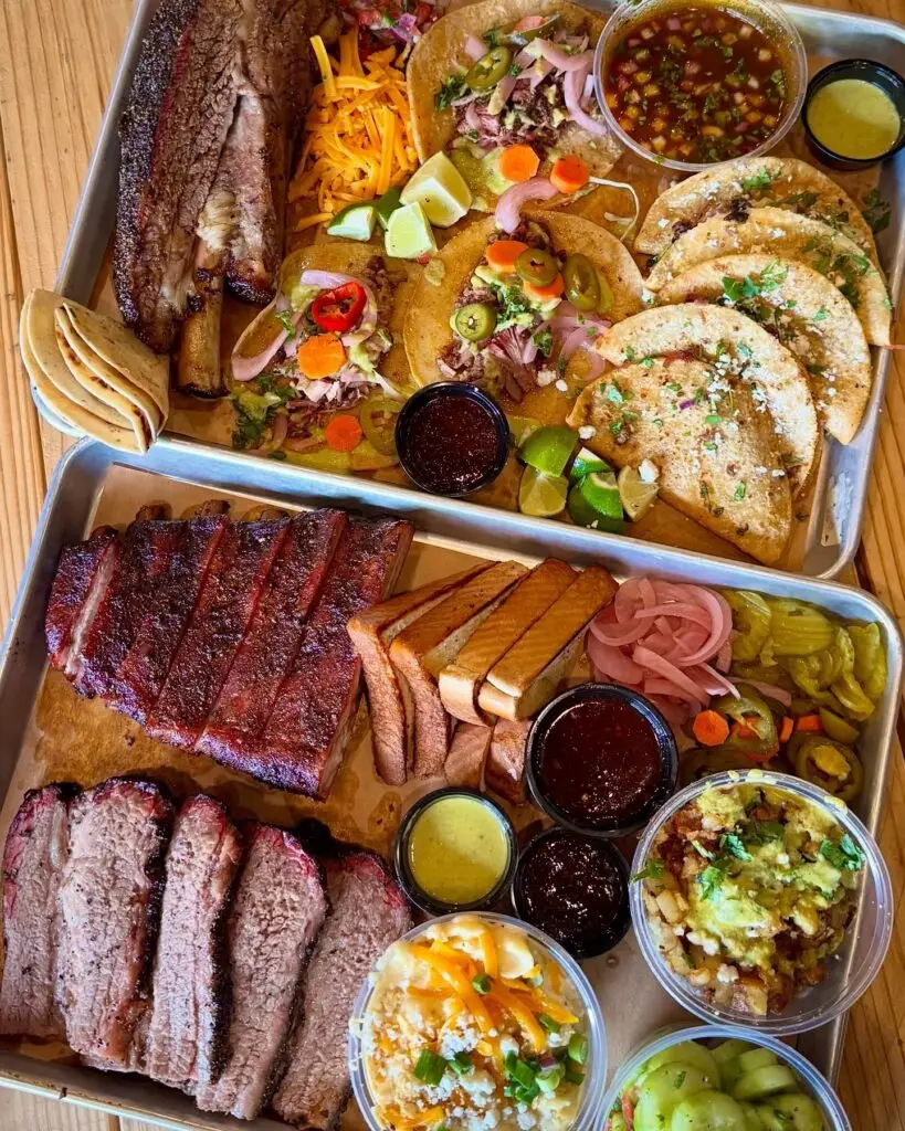 Large barbecue spread from Vaqueros Texas Bar-B-Q featuring brisket, ribs, tacos, queso, and smoked meats.
