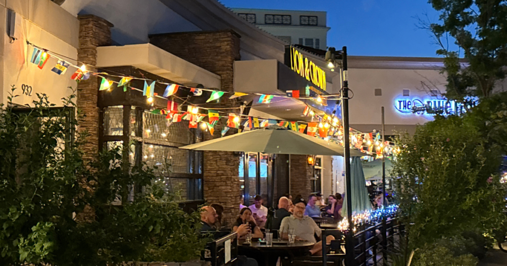 Outdoor patio dining at Watters Creek Village in Allen, Texas, featuring string lights, international flags, and guests enjoying the evening.