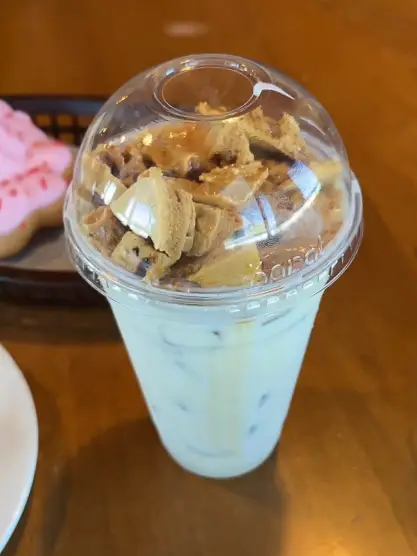 An iced dalgona candy latte coffee topped with whipped coffee and cookie pieces sits on a table at Caffe Promenade in Allen, Texas.