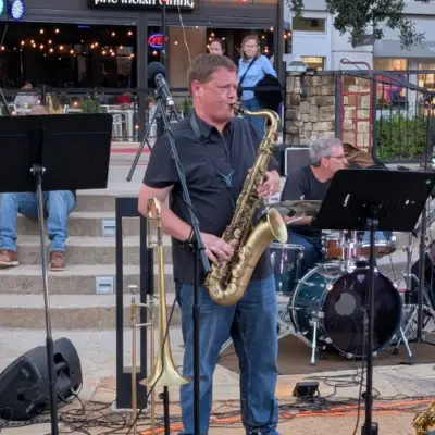 A saxophone player performs with Last Call featuring The Top Shelf Brass during Concerts by the Creek at Watters Creek Village in Allen, Texas, as the band entertains guests outdoors.