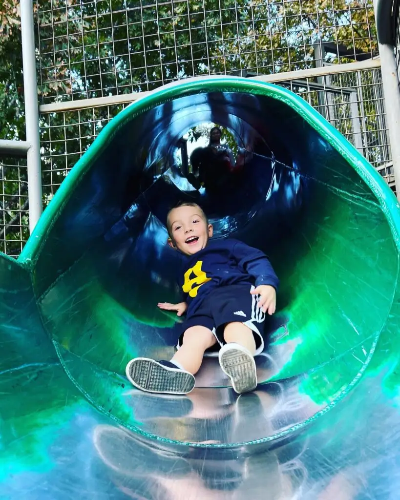 A child smiles while sliding down the slide at Watters Creek Village treehouse play area.
