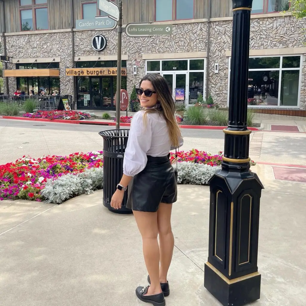 A visitor strolls through Watters Creek Village in Allen, Texas, with colorful flower beds and Village Burger Bar visible in the background.