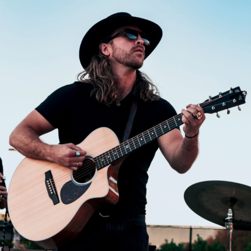 Clayton Stewart performs on acoustic guitar while wearing a black cowboy hat and sunglasses.