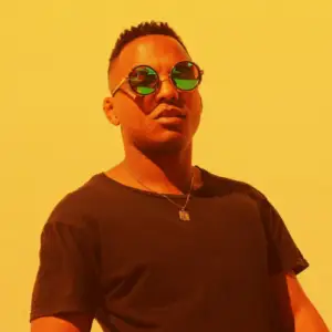 Portrait of musician Larry Ladale wearing round sunglasses against a vibrant yellow background.