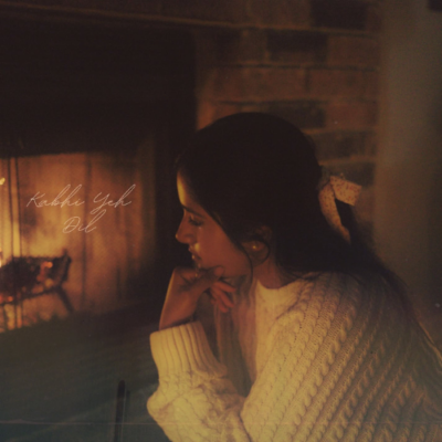 Singer-songwriter Pri sits beside a fireplace wearing a cream cable-knit sweater.
