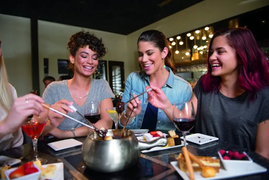 Friends smile and enjoy cheese and chocolate fondue together at The Melting Pot in Allen.