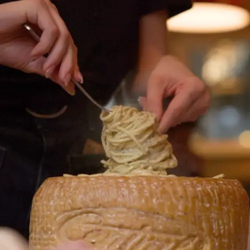 Server twirling pasta above a wheel of Parmesan cheese at Numero 28 in Allen, Texas.