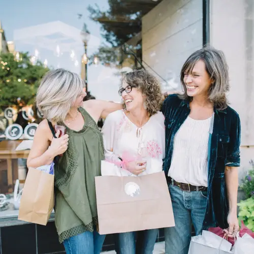 Three women carrying shopping bags and laughing together while shopping in Allen, Texas.