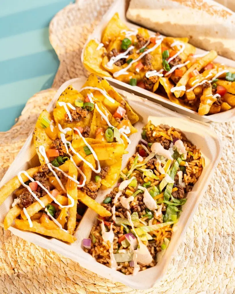 Trays of loaded fries and a rice bowl from Barrio Burrito Bar topped with seasoned ground beef, cheese sauce, lettuce, tomatoes, green onions and creamy sauces.
