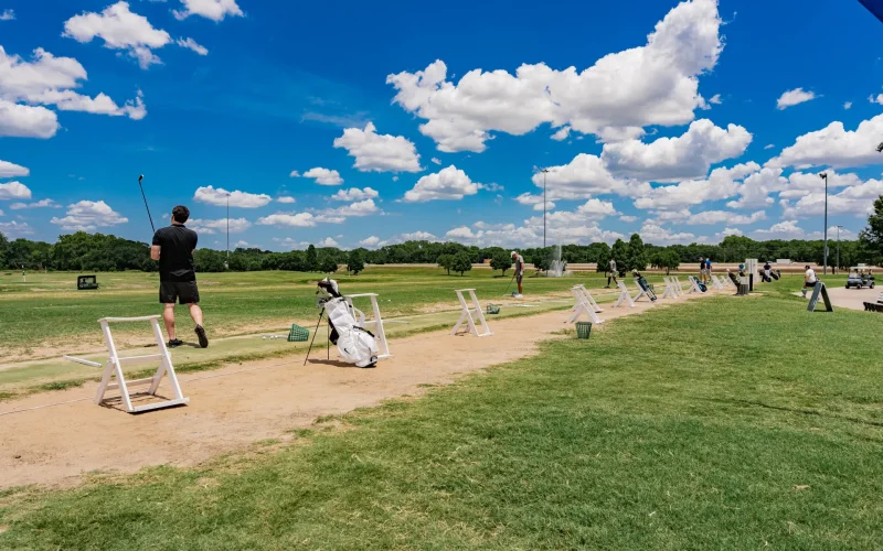 Golfers practicing at a driving range at The Courses at Watters Creek in Allen, Texas under a blue sky.